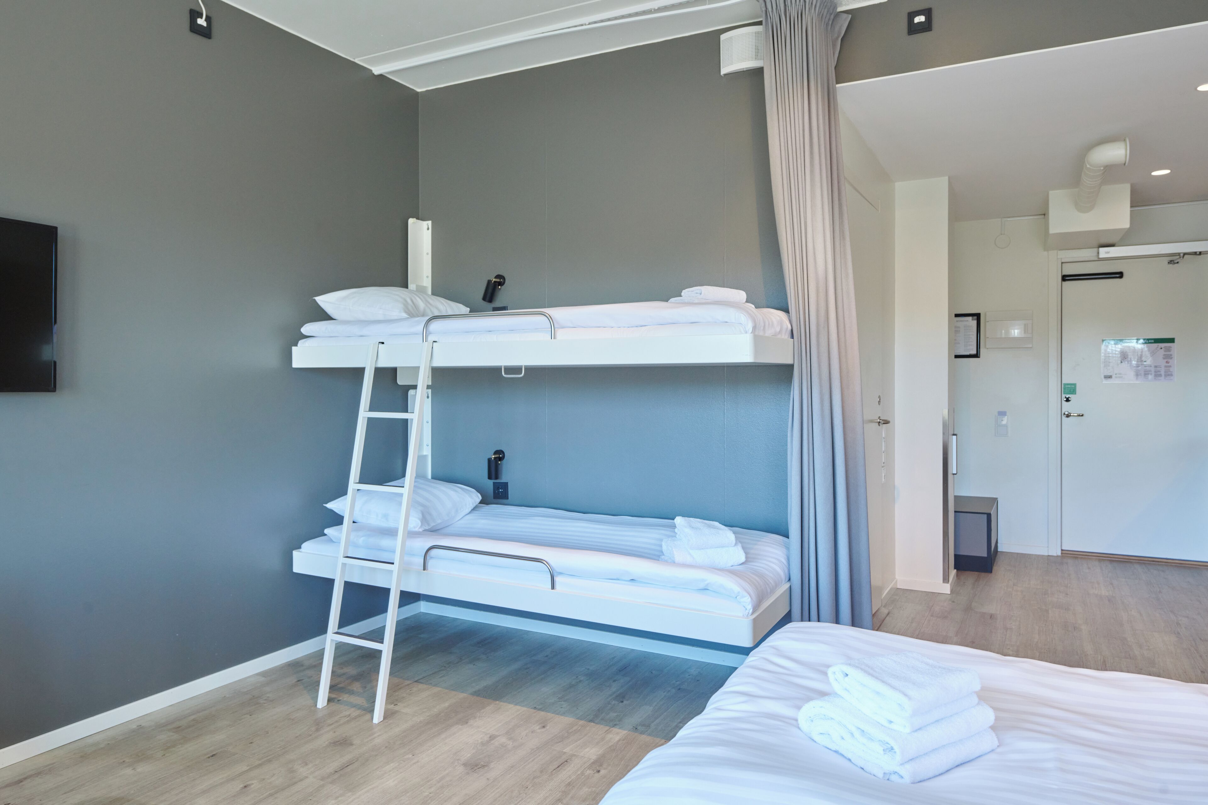 Una habitación de hotel con literas, una mesita de noche, una lámpara y una puerta que da a un baño.