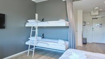 Una habitación de hotel con literas, una mesita de noche, una lámpara y una puerta que da a un baño.