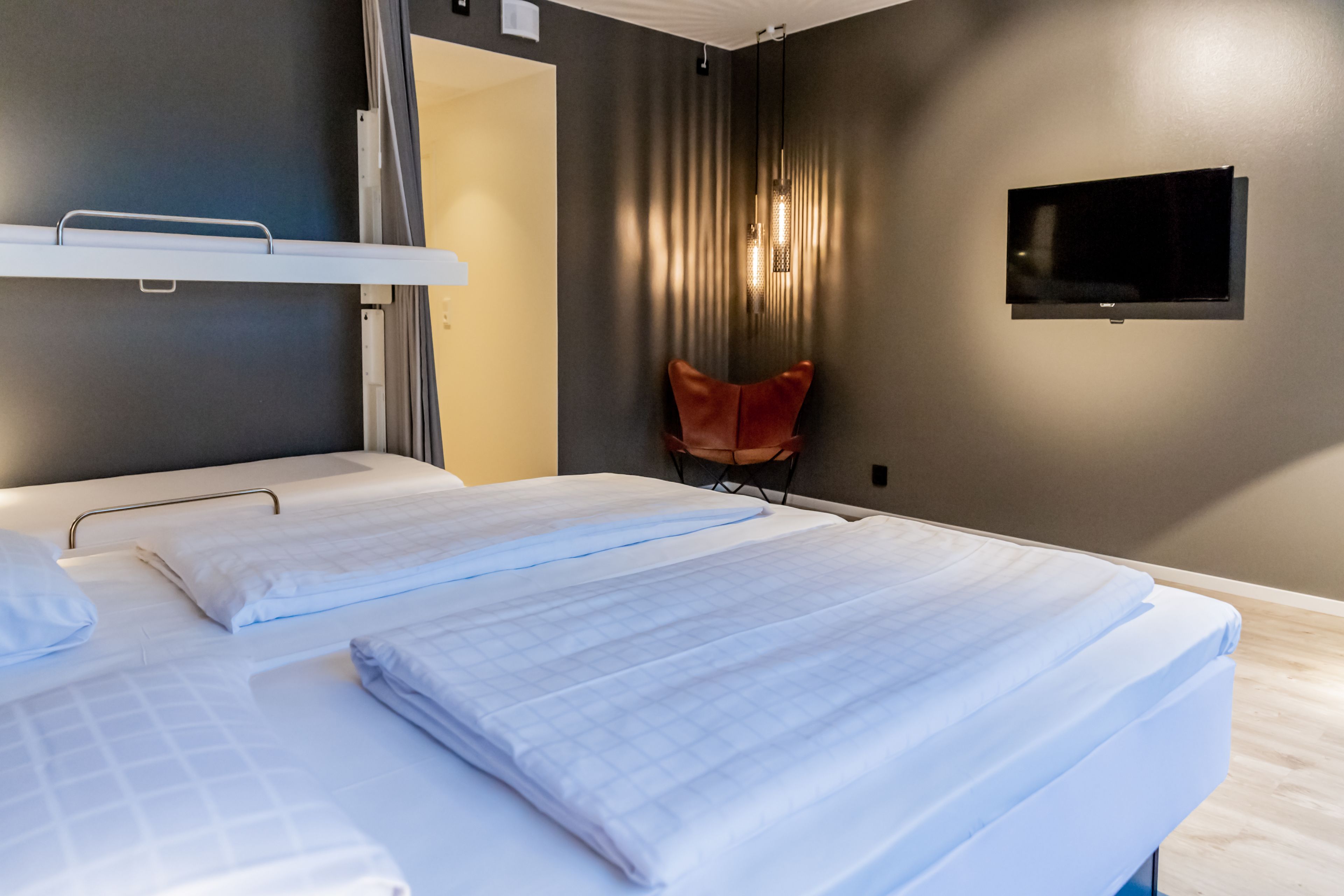 Une chambre d’hôtel avec deux lits, un téléviseur fixé au mur et une chaise rouge.