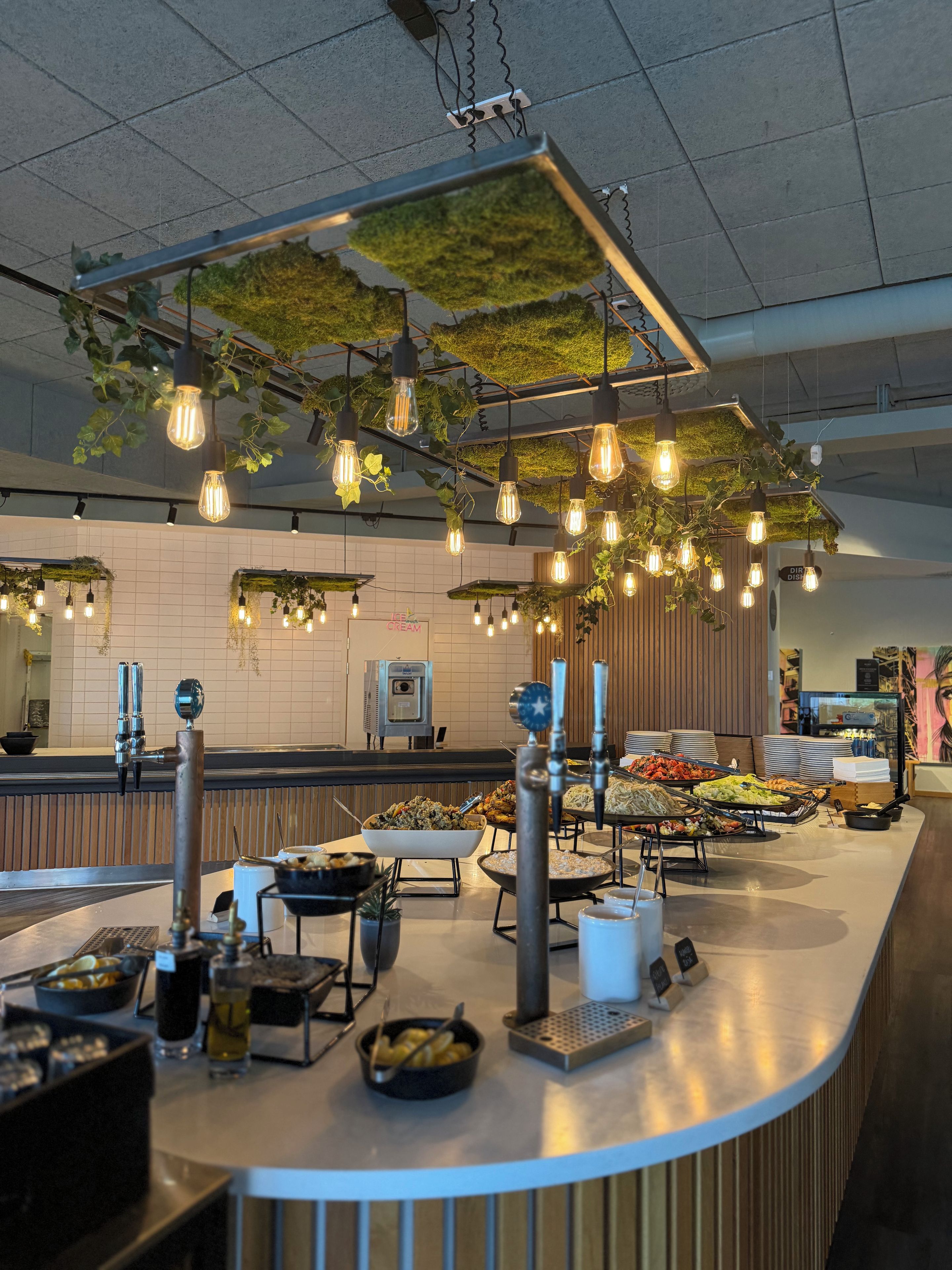 Zona de bufé con diversas opciones de comida, estación de café y lámparas colgantes.