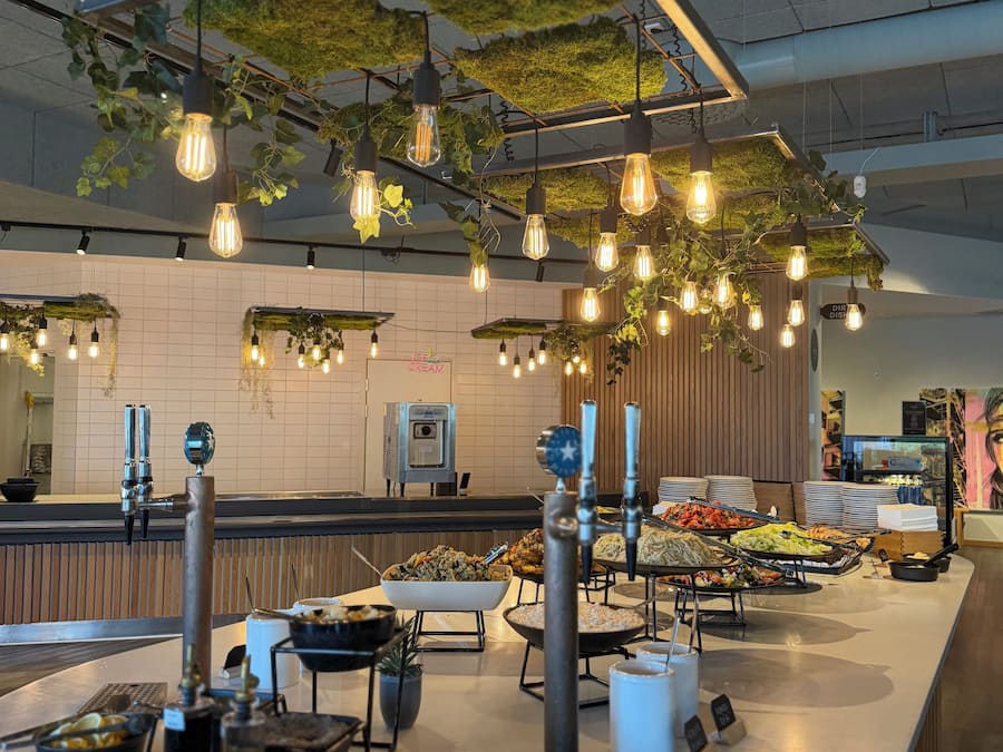 A buffet area with a variety of food options, a coffee station, and hanging light fixtures.