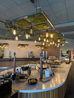 Un espace buffet proposant une variété de plats, un coin café et des luminaires suspendus.