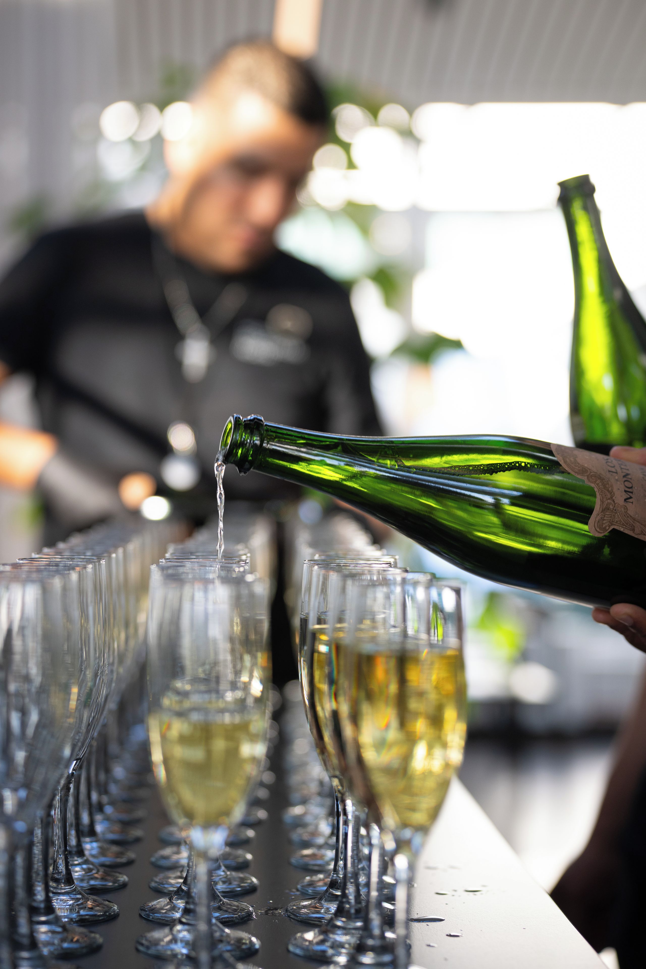 A person pouring a clear liquid from a green bottle into a glass.