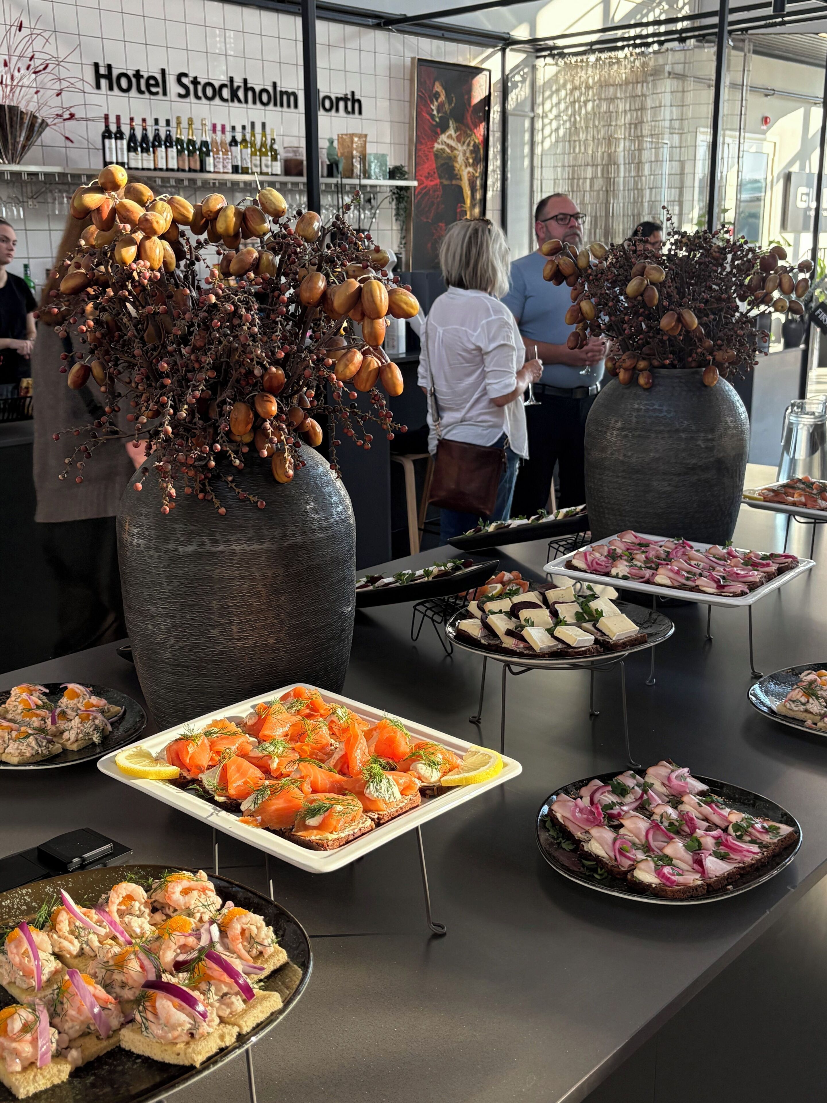 Un buffet proposant une variété de plats, notamment des amuse-gueules à base de saumon et de crevettes, ainsi que des vases décoratifs ornés de branches séchées.