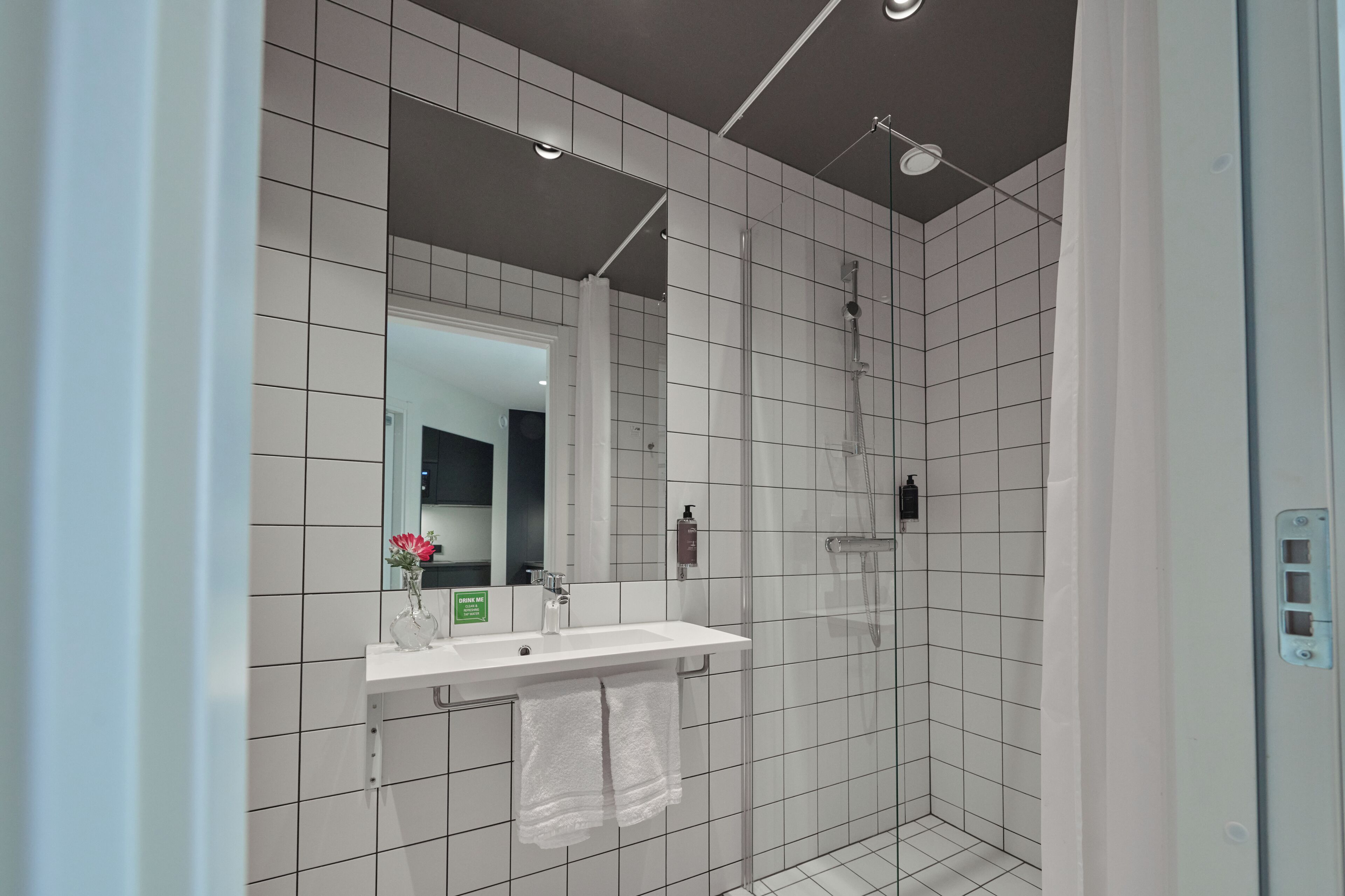 A modern bathroom with a white tiled shower, a sink with a mirror, and a towel hanging on the wall.