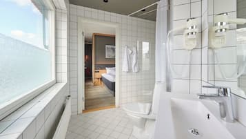 Un baño moderno con azulejos blancos, un ventanal grande, una ducha con cabezal de ducha manual y un lavamanos con espejo.