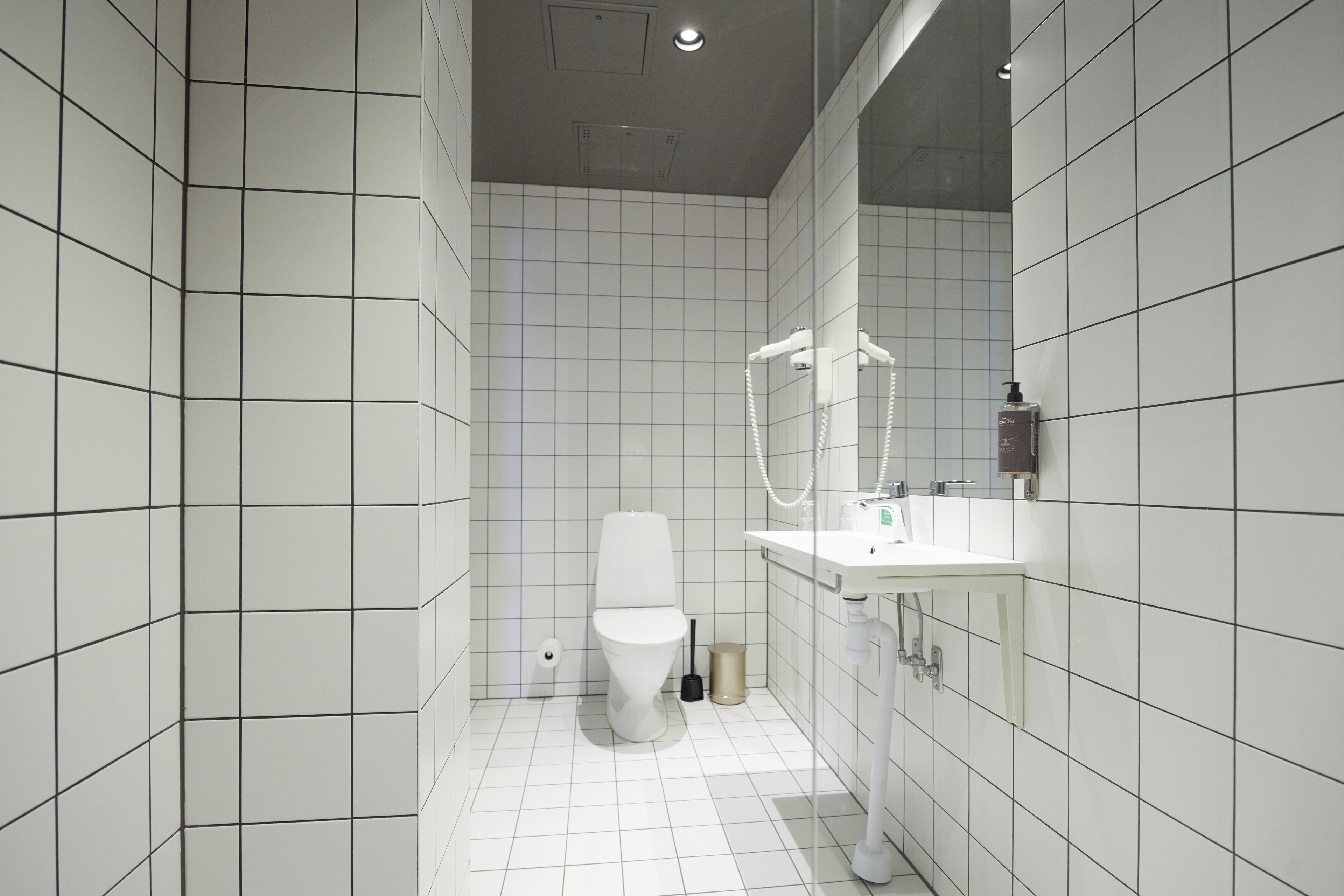 A modern bathroom with white tiled walls, a toilet, a sink, and a shower area.