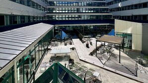 Un edificio moderno con varios pisos, amplias ventanas y un patio central con mesas al aire libre.