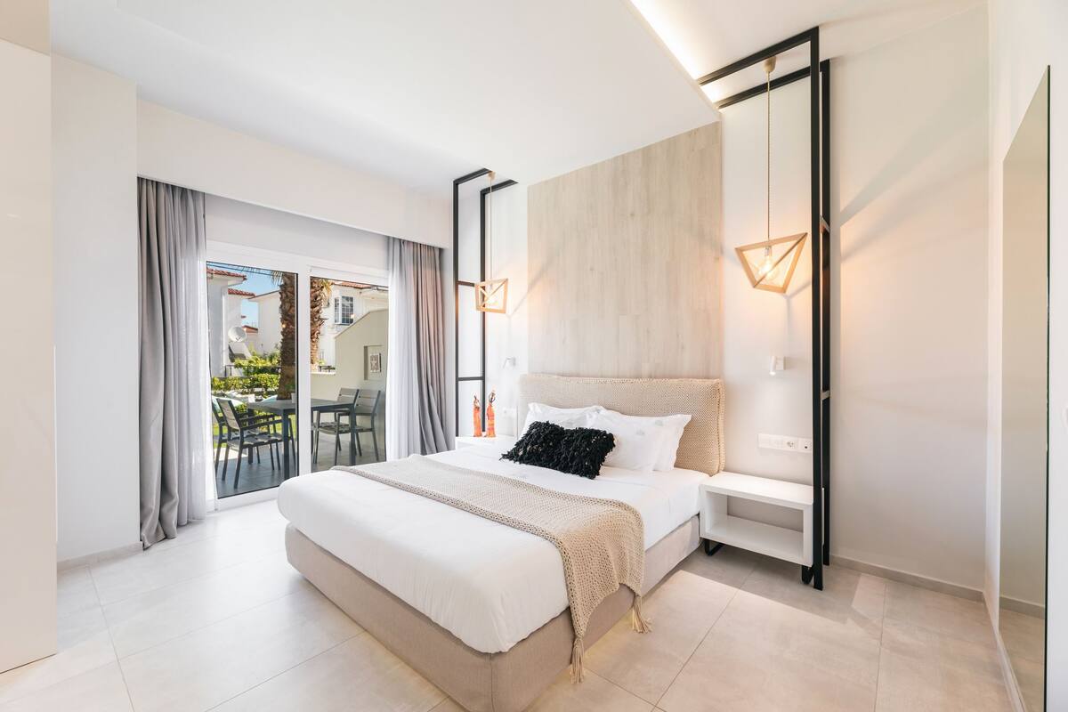 Quarto moderno com uma cama grande, uma mesa de cabeceira e vista para o exterior.