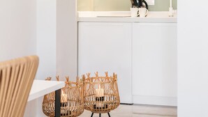 A modern kitchen with white cabinets, a stainless steel range hood, and a dining area with a white table and wicker chairs.