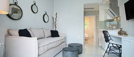A modern living room with a sofa, two round ottomans, a black chair, and a kitchen area with a TV.