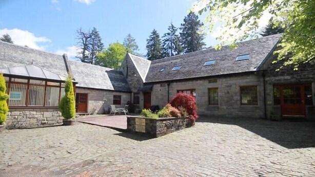 A courtyard with stone buildings, a small garden, and a cobblestone path. - Auchenheglish Lodges - The Coachhouse (Alexandria)