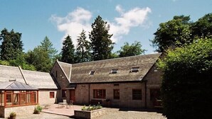 A traditional stone building with a sloped roof, a covered patio area with seating, and a small garden. - Auchenheglish Lodges - The Coachhouse (Alexandria)
