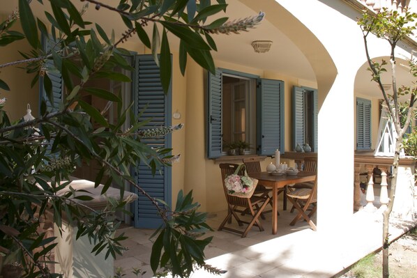 A covered outdoor dining area with a table and chairs, blue shutters, and a potted plant. - Relais & Residence Villa Mazzanta (Rosignano Marittimo)