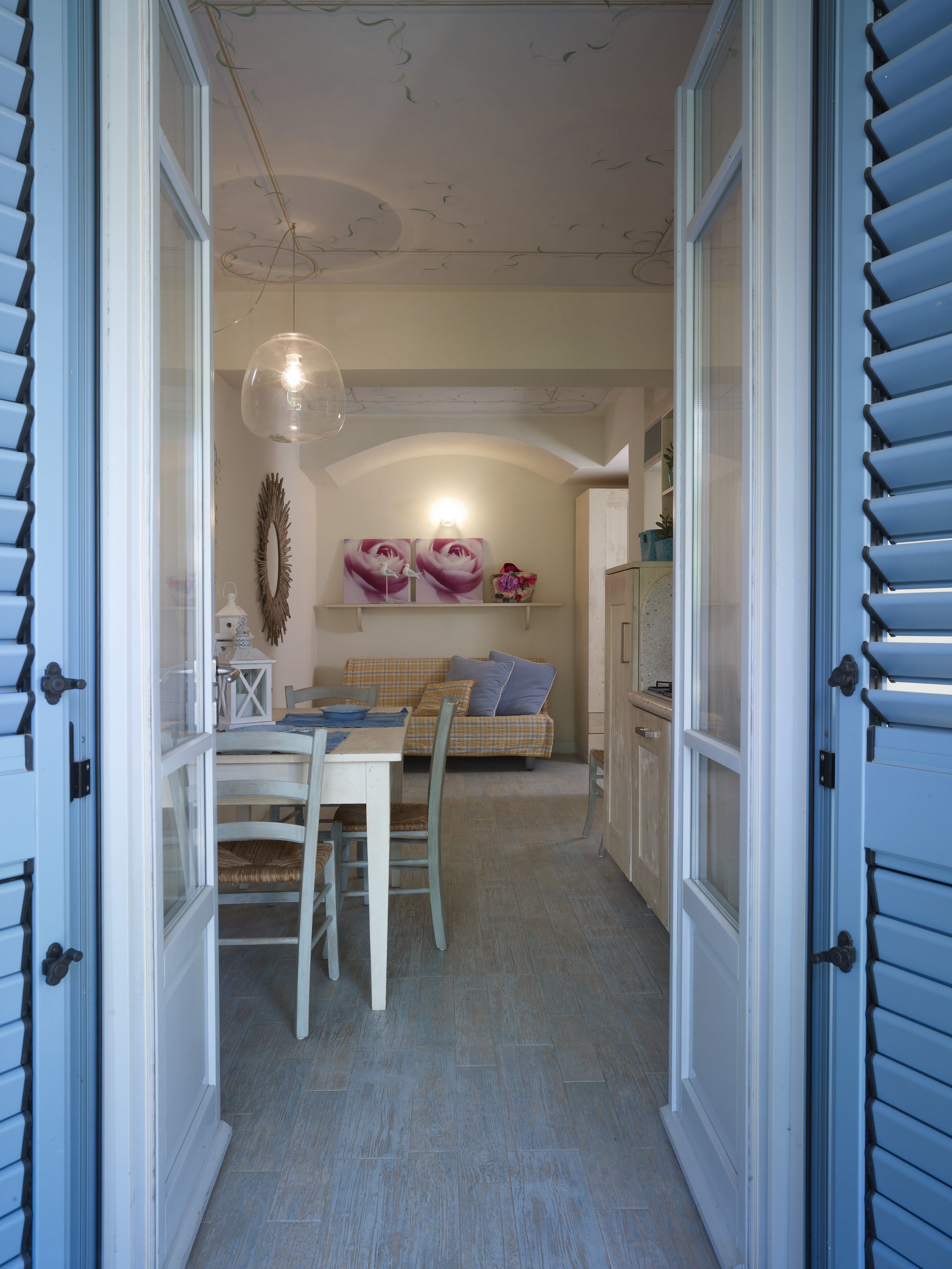 An open doorway leading to a dining area with a table and chairs, a hanging light fixture, and a sofa with cushions.
