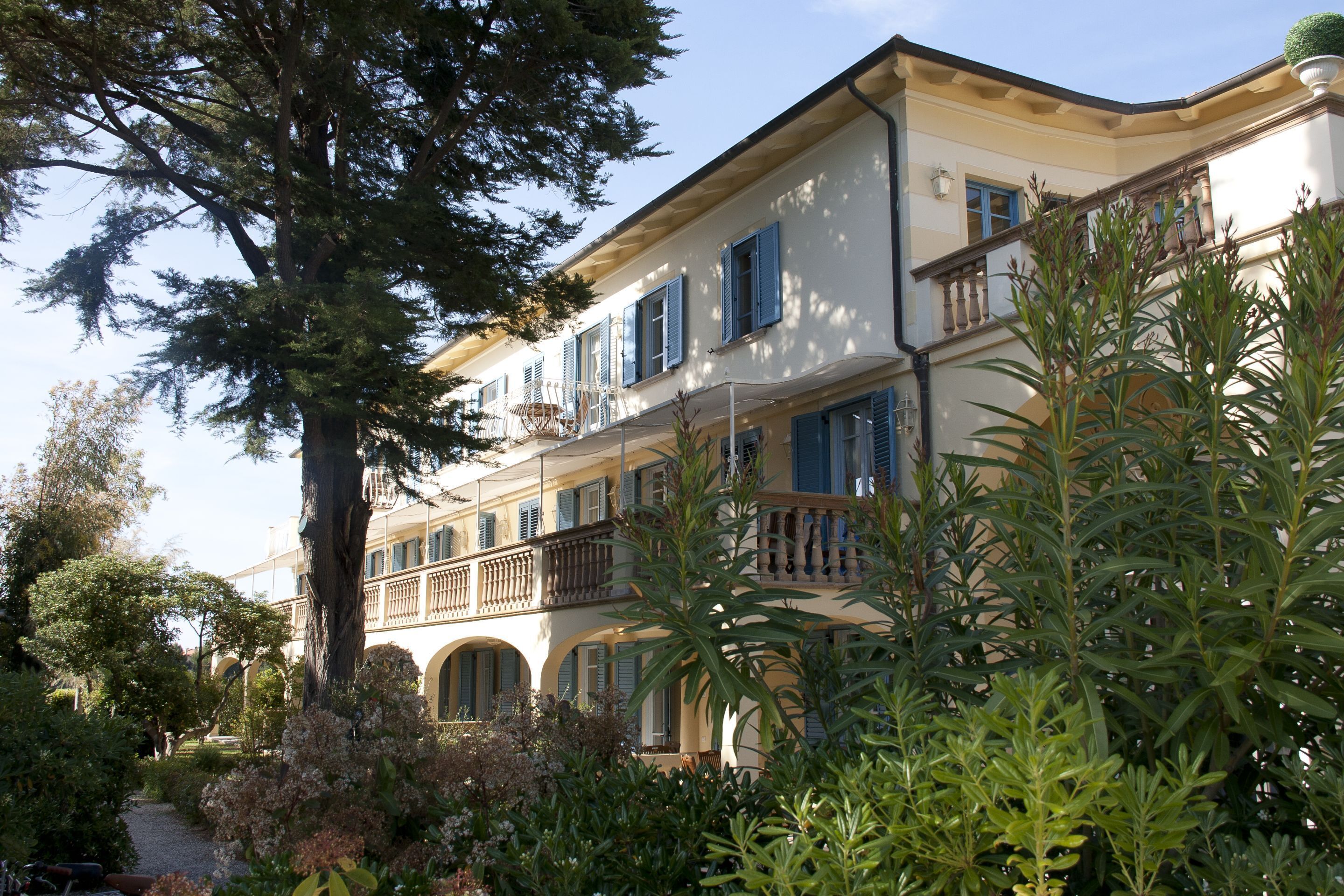 Un immeuble à plusieurs étages, doté de balcons et de fenêtres en arc de cercle, entouré d’une végétation luxuriante et d’arbres.