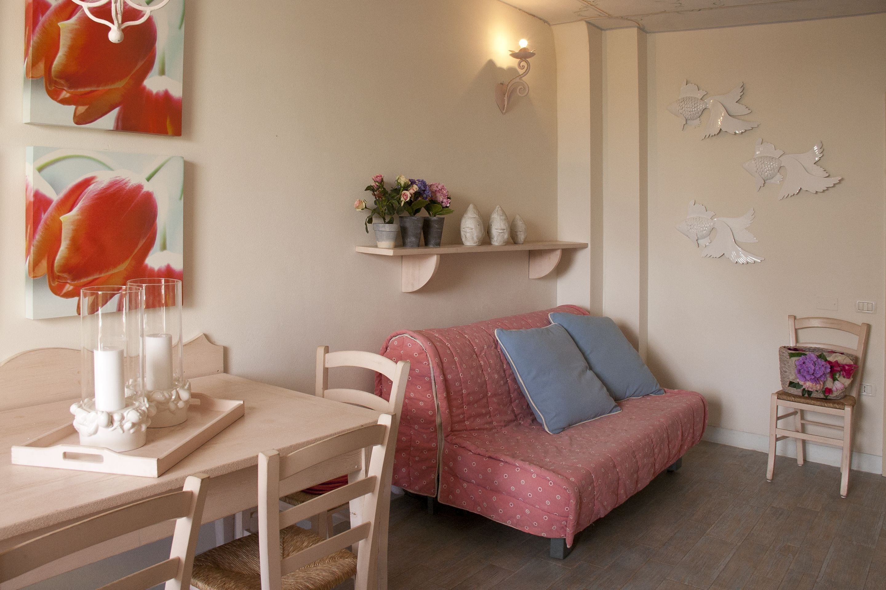 A cozy room with a wooden table, a pink sofa with blue cushions, and a small side table with decorative items.