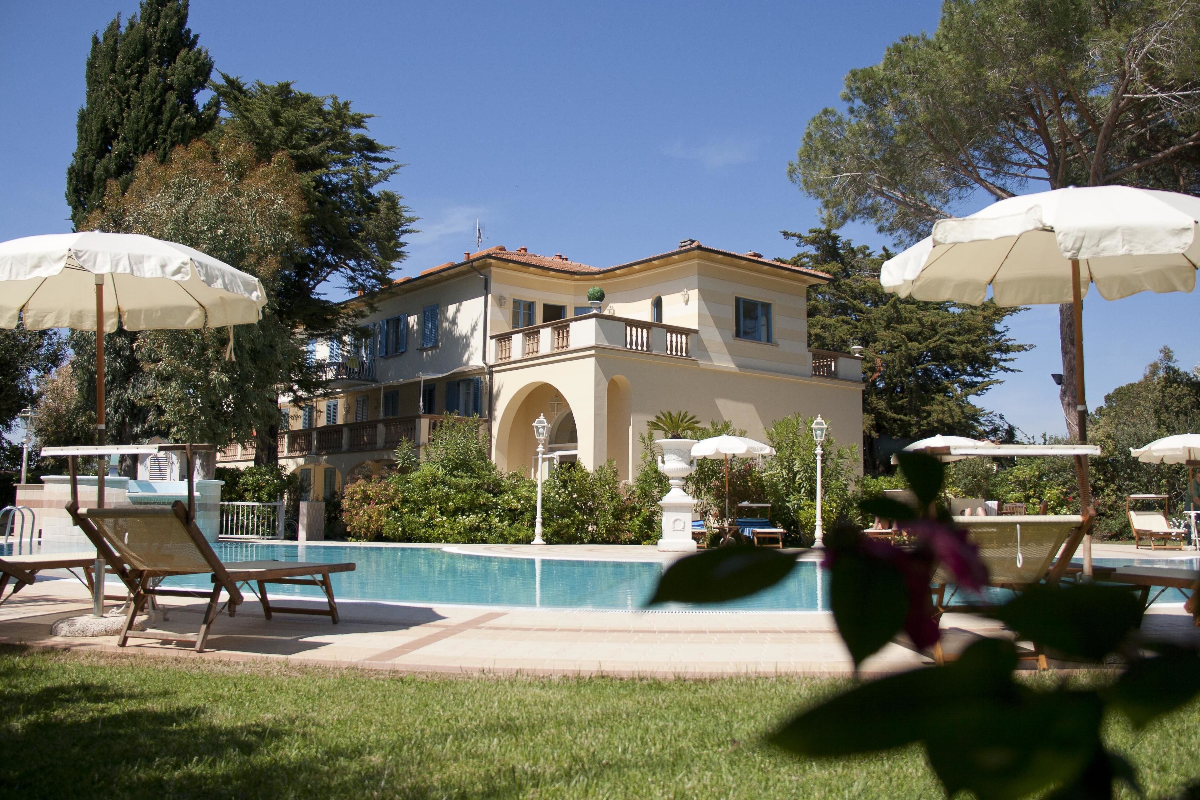 A pool area with lounge chairs and umbrellas, a building with a balcony, and a clear blue sky.