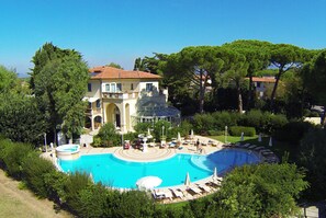 A large, circular swimming pool surrounded by lush greenery, with a building featuring a dome and multiple balconies in the background. - Relais & Residence Villa Mazzanta (Rosignano Marittimo)
