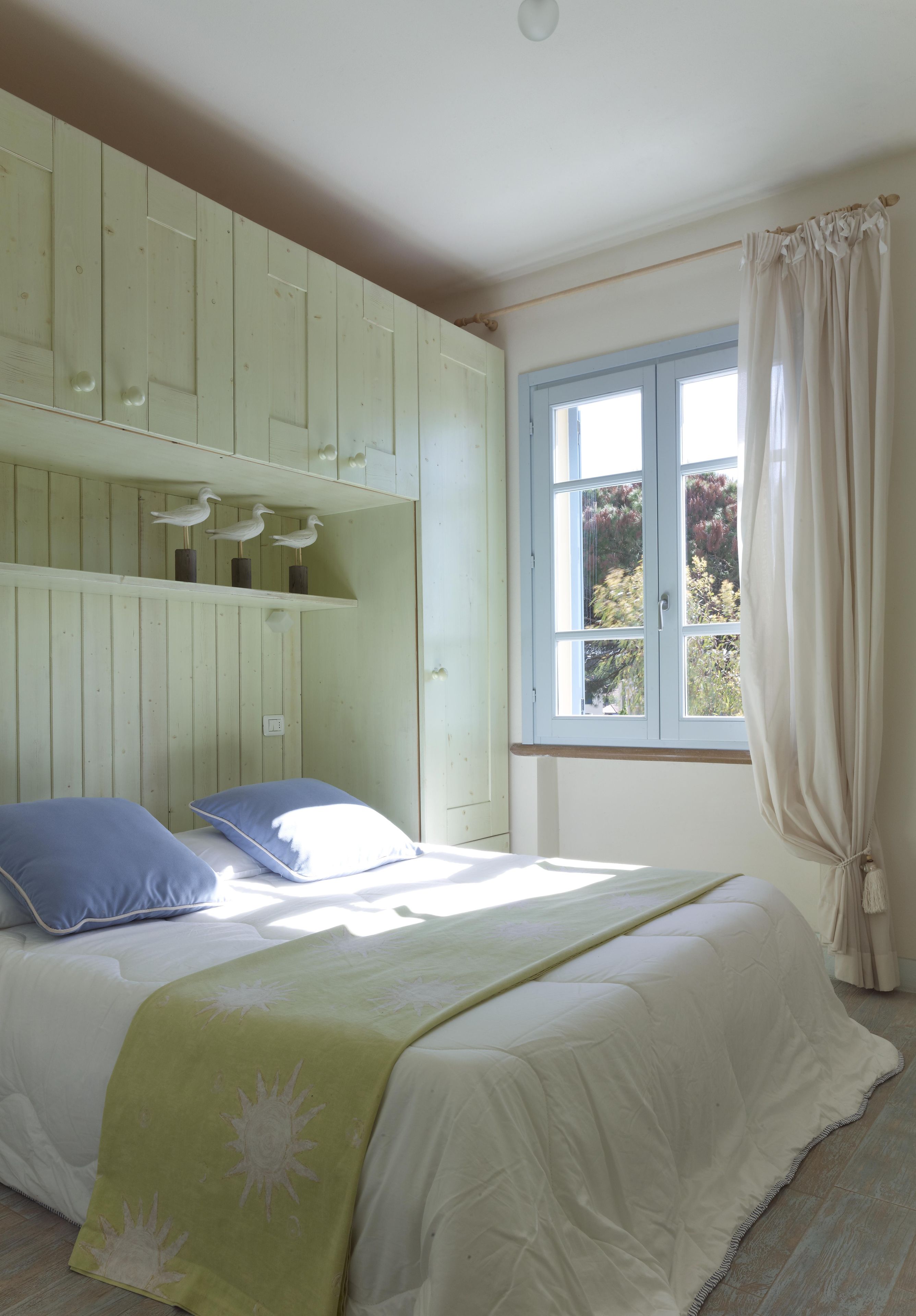 A bedroom with a bed, a window with curtains, and a shelf with decorative items.