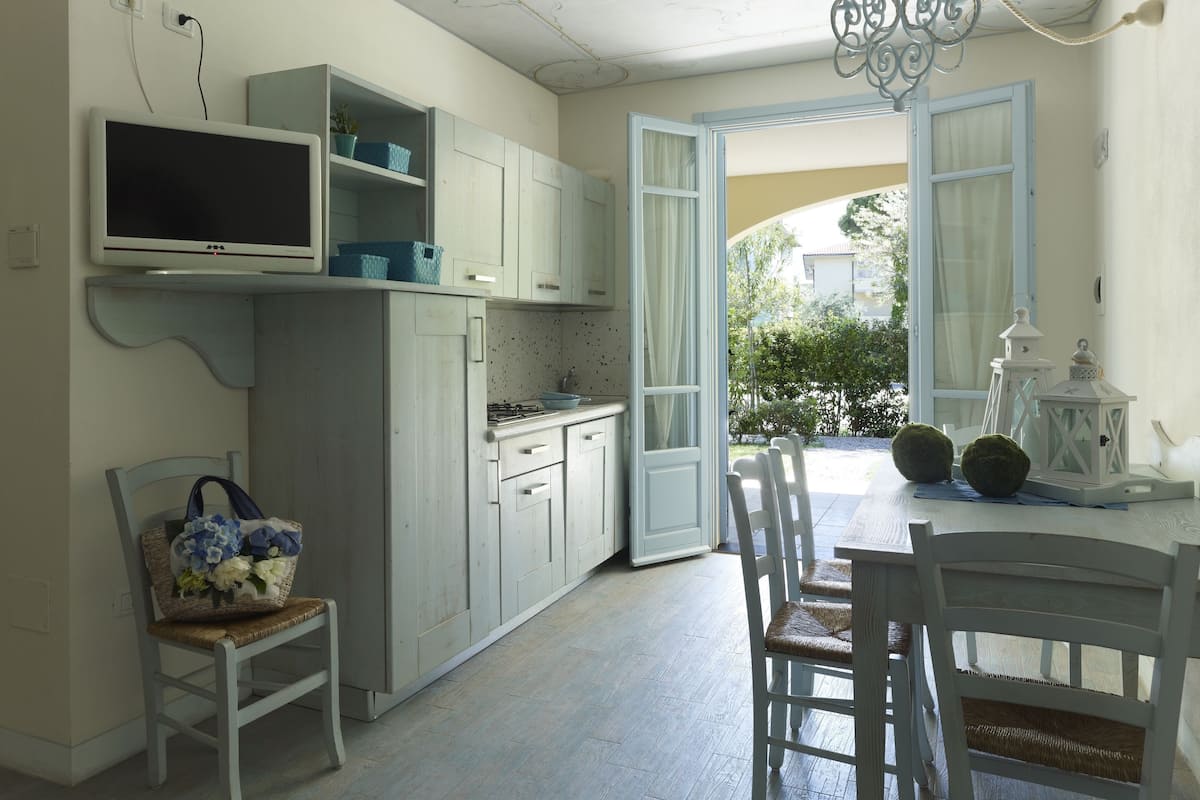 A kitchen with white cabinets, a TV, and a dining area with a table and chairs.