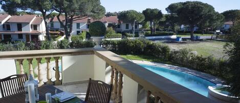 A dining area with a table set for four, overlooking a swimming pool and a residential area with houses and trees.