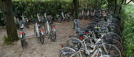 Un aparcamiento para bicicletas con varias bicicletas alineadas junto a árboles y una cerca.