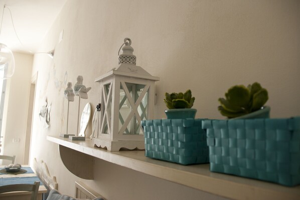 Una estantería con adornos, incluyendo un farol blanco, figuritas y dos macetas azules con textura y plantas verdes.