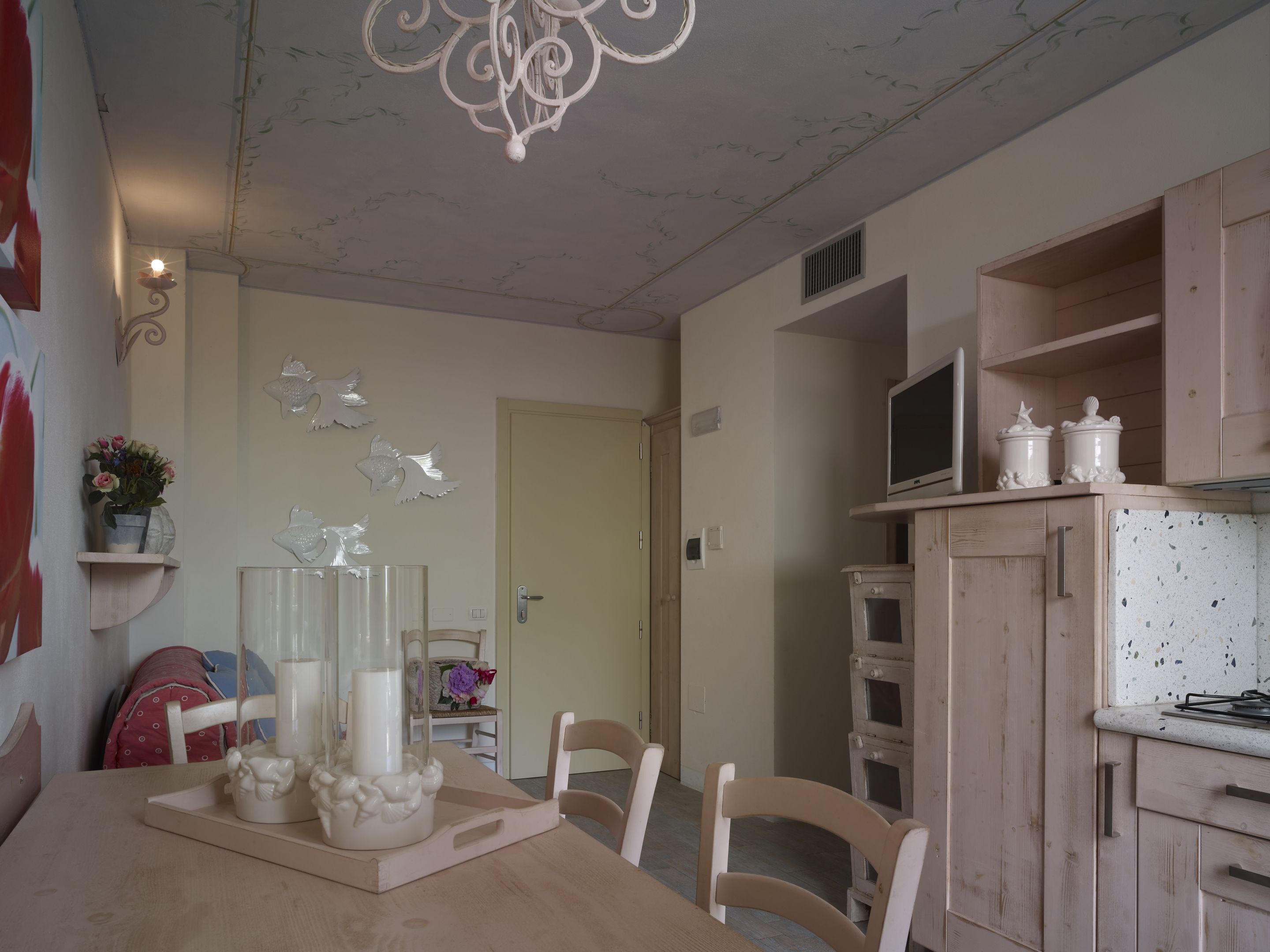A dining area with a wooden table, chairs, a chandelier, and a kitchen with wooden cabinets and appliances.