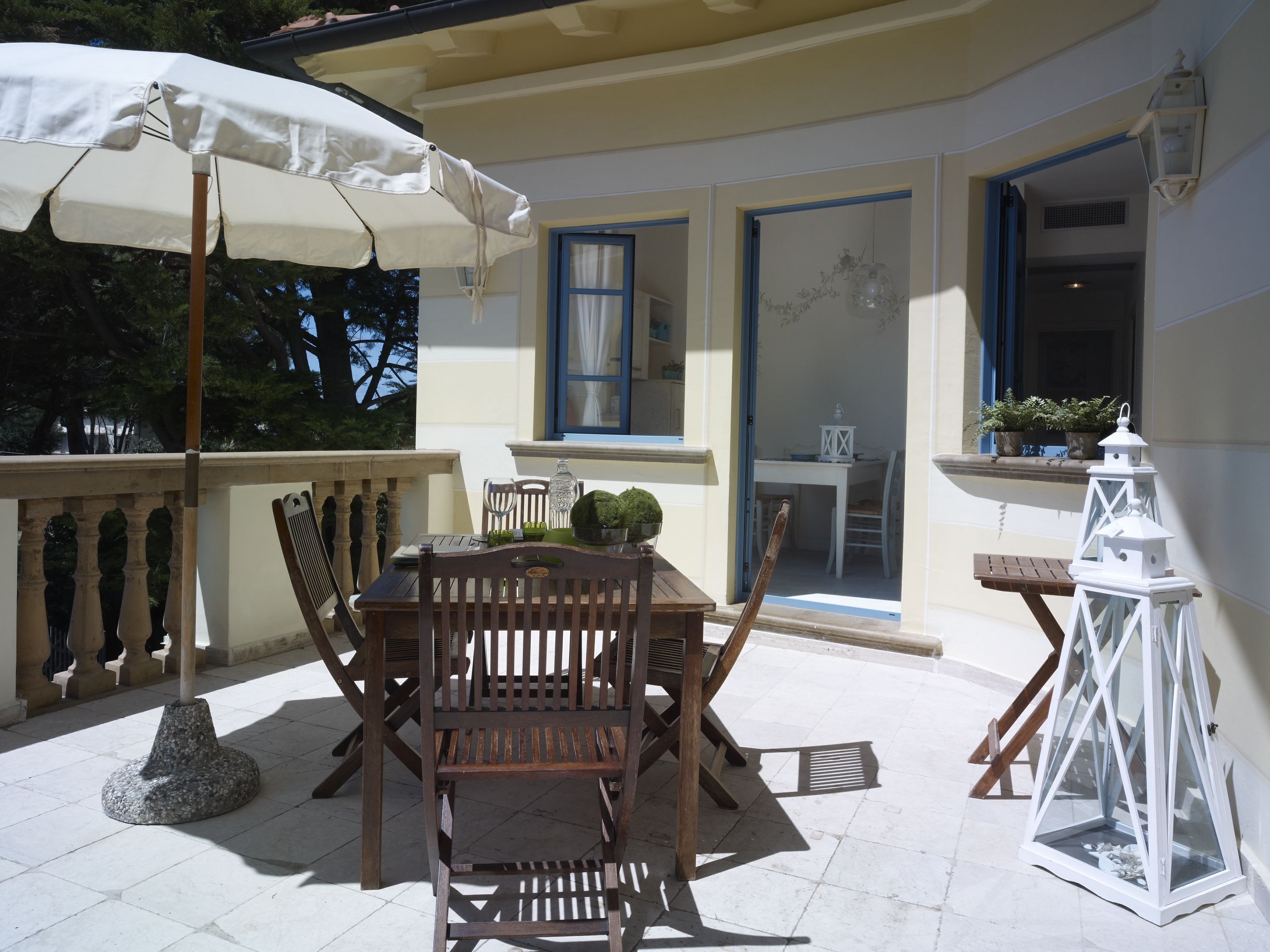 Un patio con un tavolo e sedie di legno, un ombrellone bianco e una lanterna bianca.