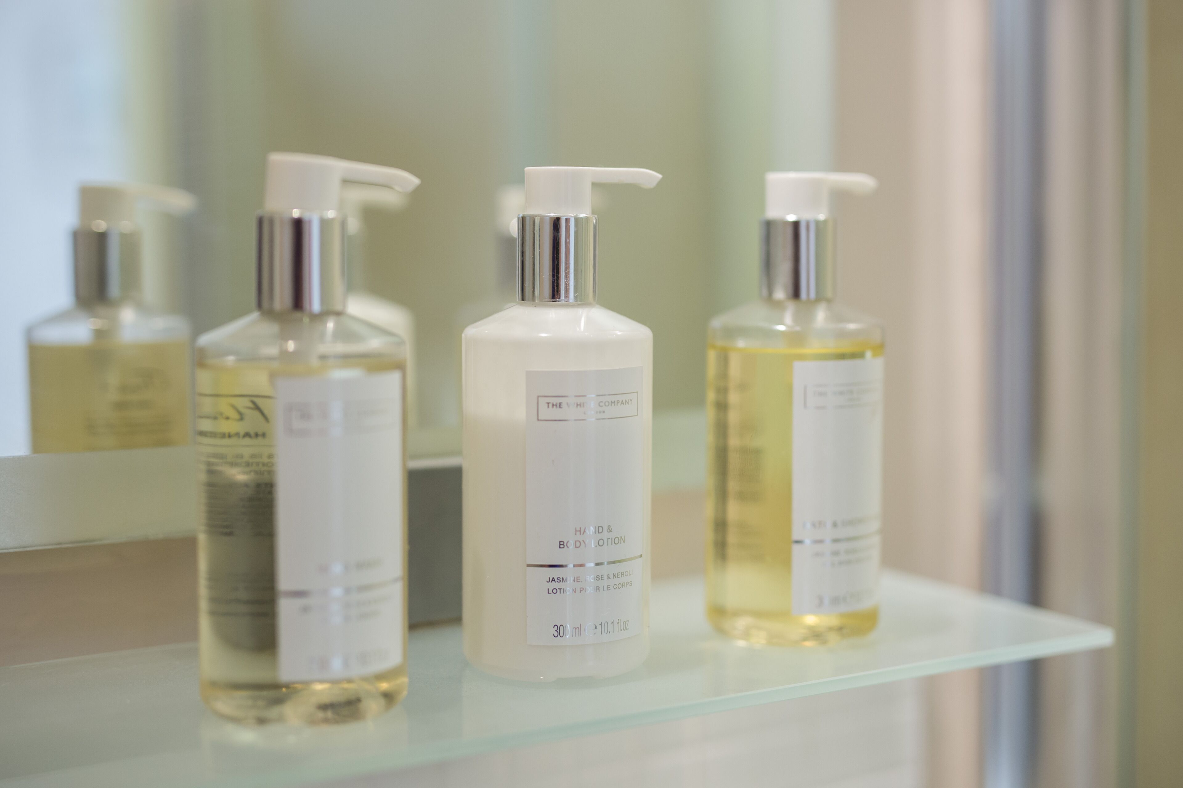 Trois flacons de lotion sont posés sur une étagère en verre dans une salle de bain.