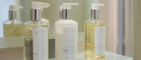 Trois flacons de lotion sont posés sur une étagère en verre dans une salle de bain.