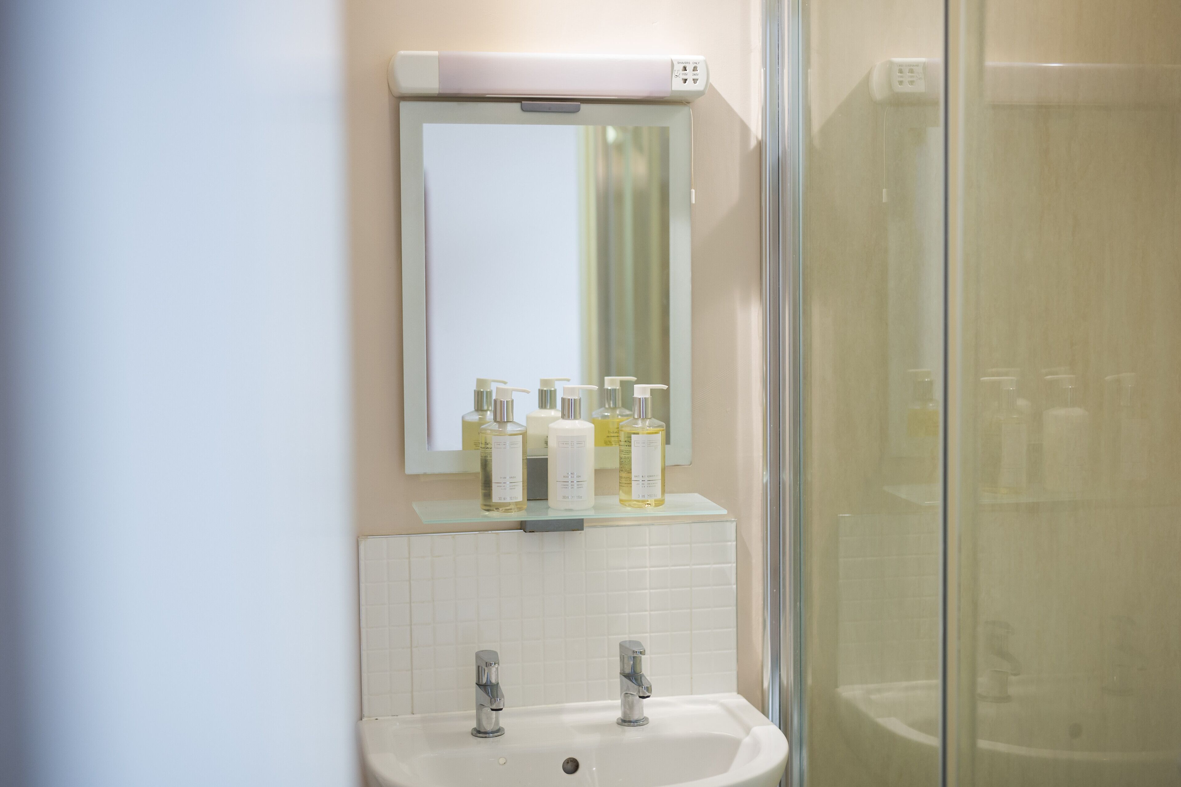 A bathroom with a white sink, two faucets, a mirror, and a glass shower enclosure.