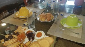 A breakfast table with various pastries, a green teapot, and a glass of juice.