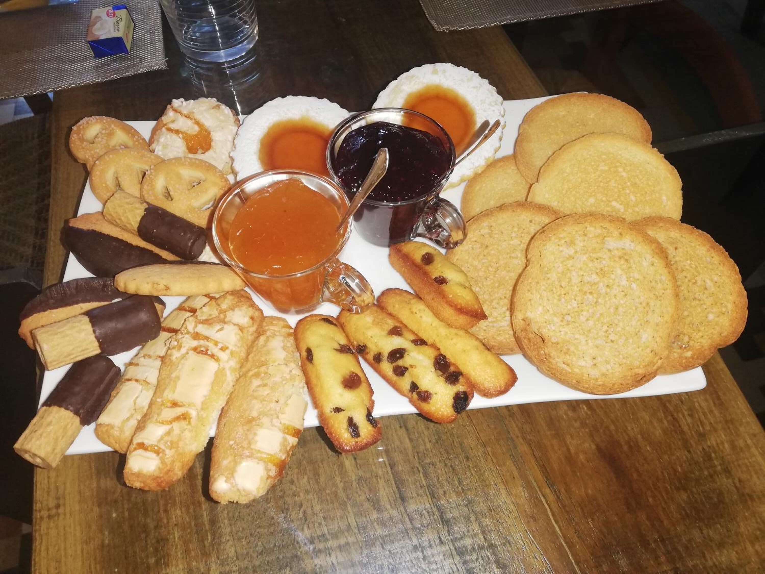 A variety of pastries and cookies on a white plate, accompanied by two glasses of syrup.