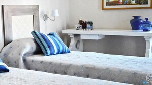 A bedroom with two beds, each with a pillow and a headboard. There is a bedside table with a lamp and a vase on it.