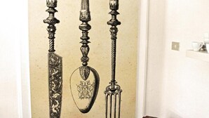 A wall with three ornate swords and a shield, a small table with a box, and a wall socket.