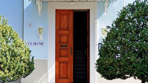 A building with a blue facade, a wooden door, and a small porch with a white railing.