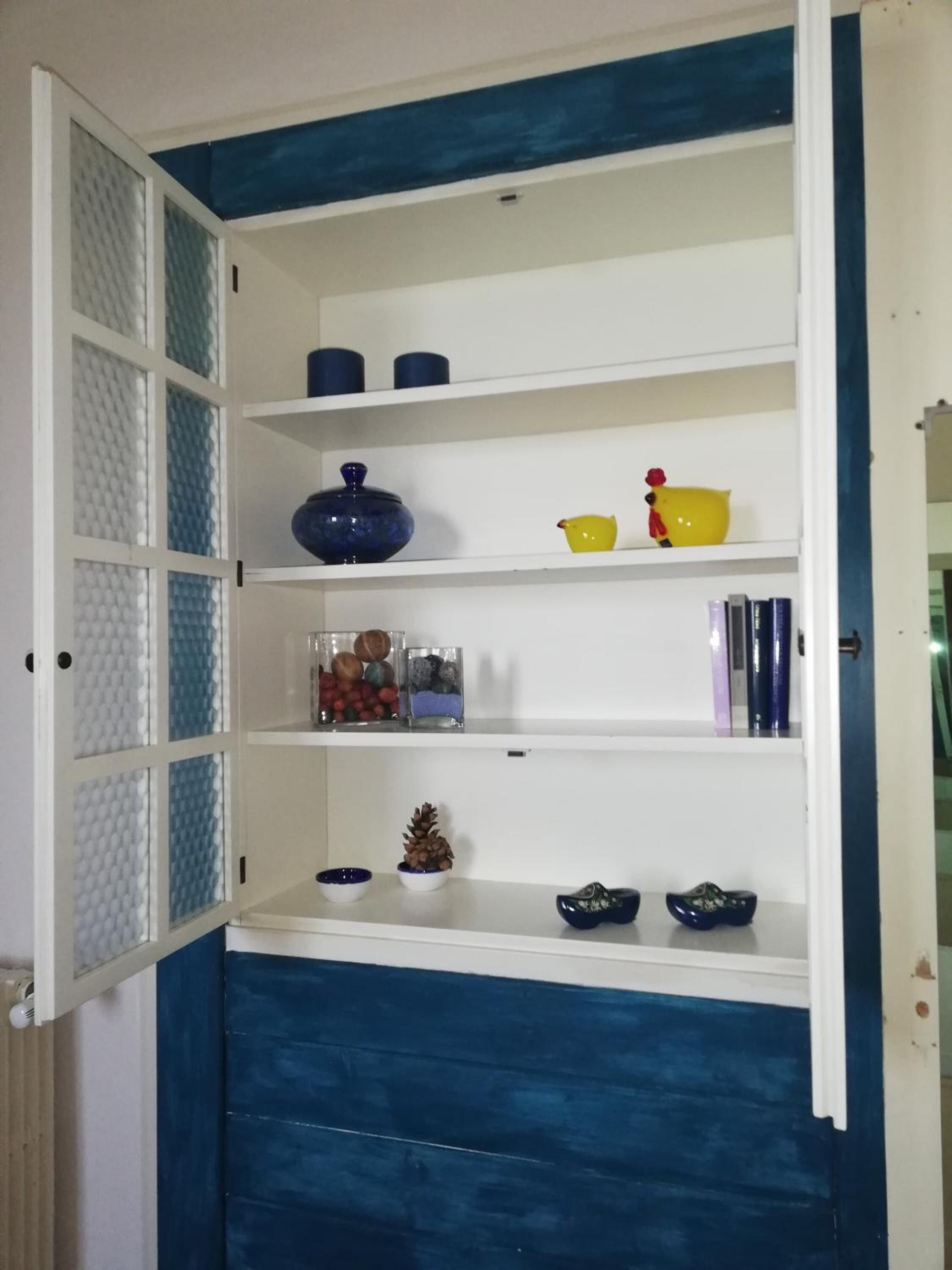 A white and blue cabinet with multiple shelves, some containing decorative items and others empty.
