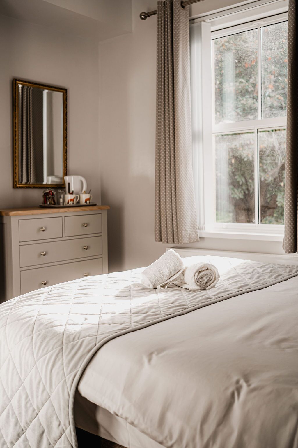 A bedroom with a bed, a dresser, a mirror, and a window with curtains.