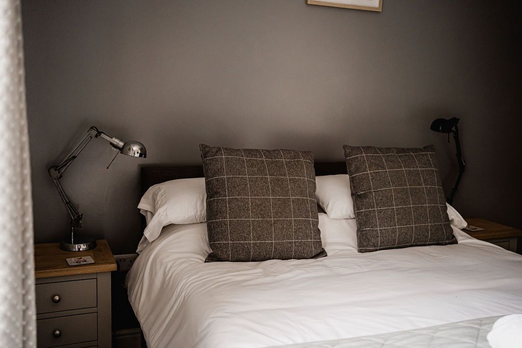 A neatly made bed with two pillows, a bedside lamp, and a nightstand with drawers.