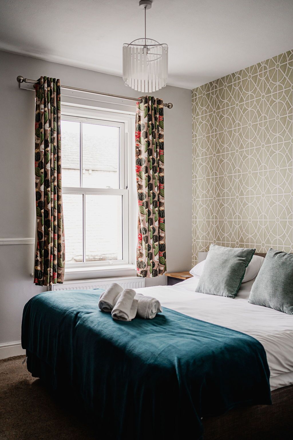 A bedroom with a bed, curtains, a window, and a patterned wall.