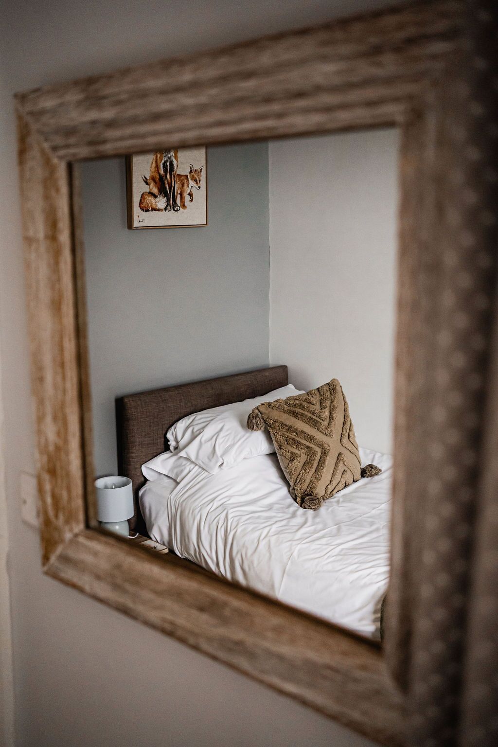 A bedroom with a bed, pillows, a bedside table with a lamp, and a framed picture on the wall.