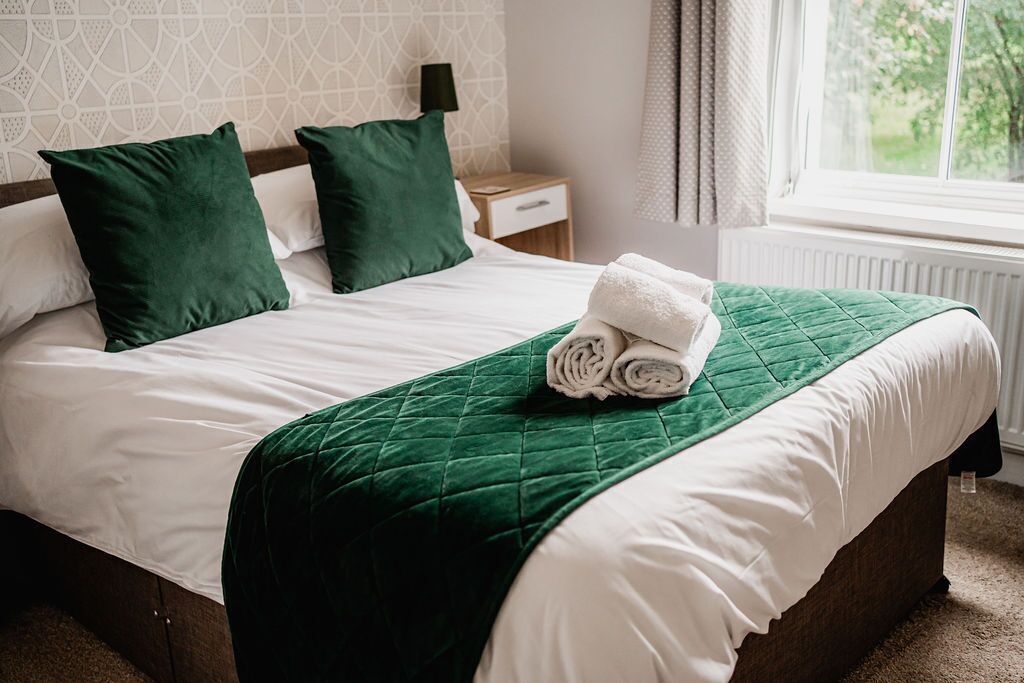 A neatly made bed with a green quilt, white linens, and two green pillows.