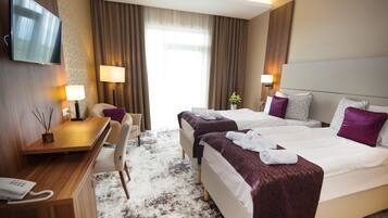 A hotel room with two beds, a desk, a chair, a TV, and a window with curtains.