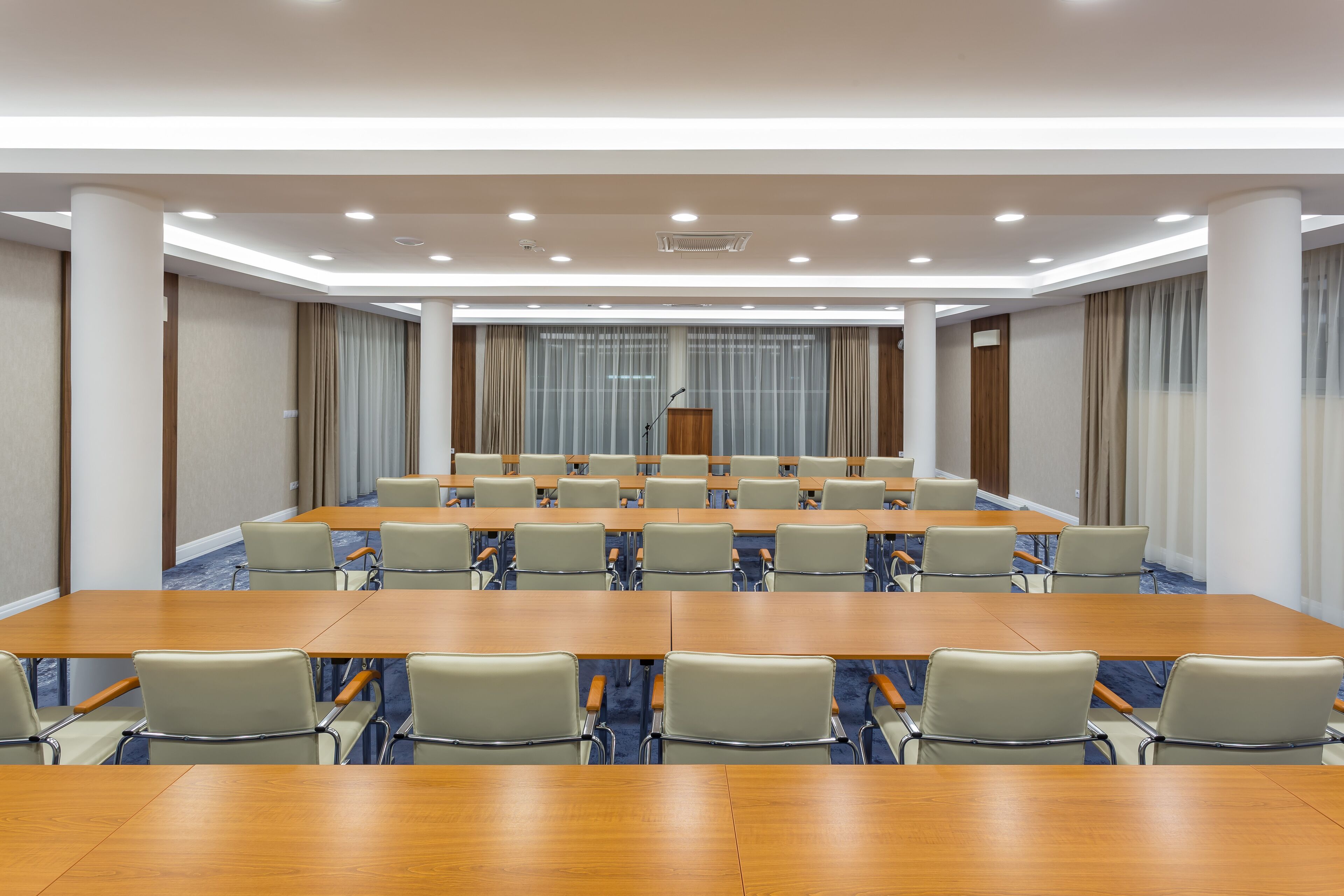 A conference room with long tables and chairs, a podium, and curtains.