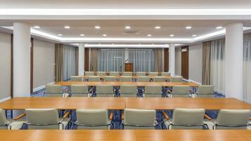Uma sala de conferências com mesas longas e cadeiras, um púlpito e cortinas.