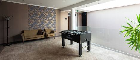 Un espacio interior moderno con mesa de futbolín, sofá y pared con diseño.