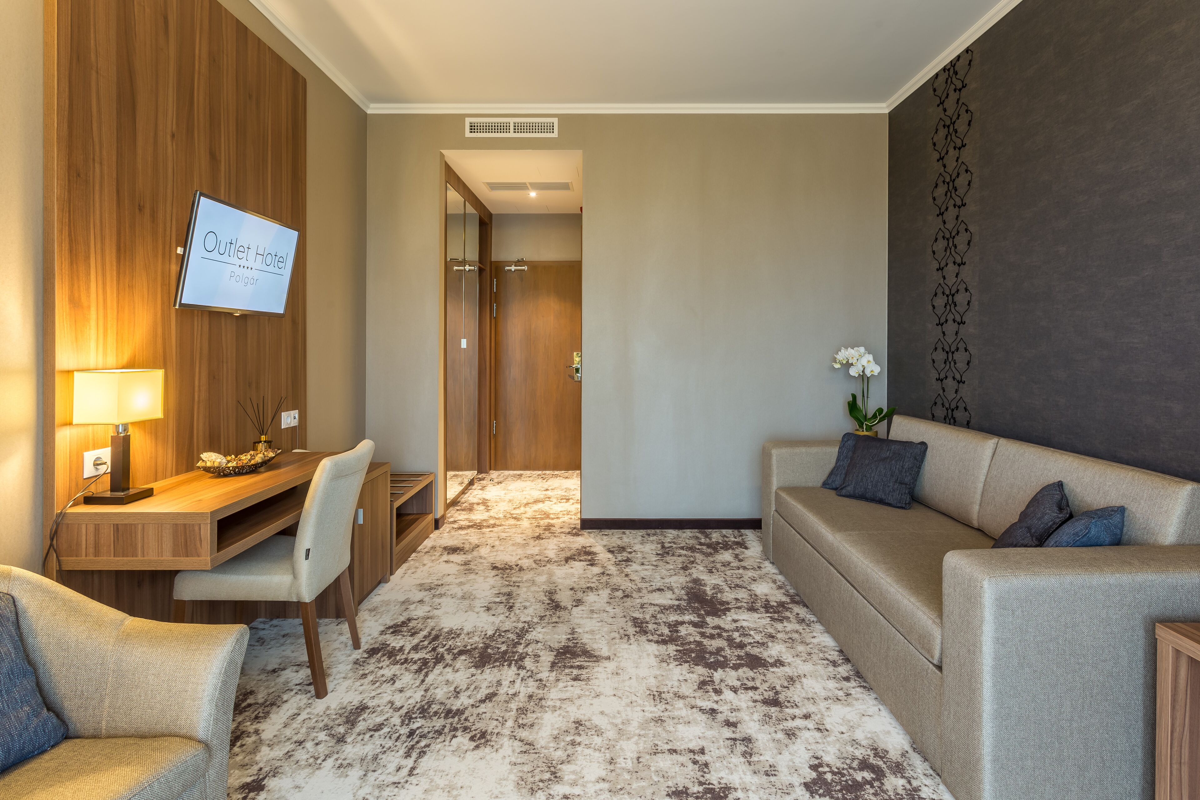 Habitación de hotel con un escritorio de madera, un sofá, un televisor y piso alfombrado.