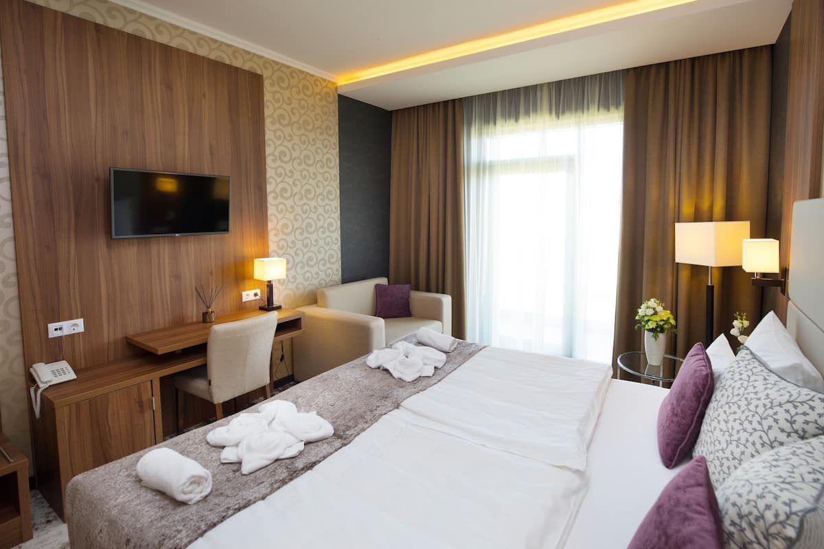 A hotel room with a bed, a desk, a chair, a TV, and a nightstand with a lamp.
